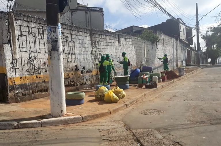 4 funcionários de uniforme verde finalizando limpeza na calçada.